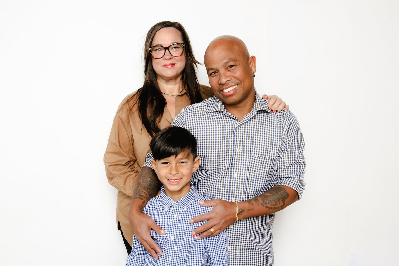 default-163 A woman stands behind a man with his arms around a boy’s shoulders as they all pose for the camera and smile.