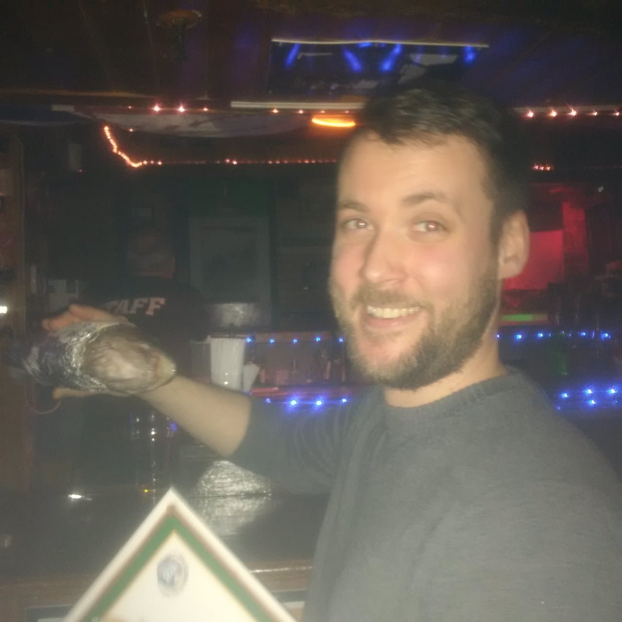 default-312 A joyful man in a bar holding a fish wrapped in foil.
