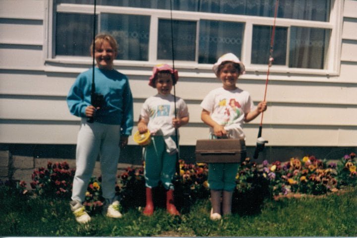 default-313 Three happy girls holding fishing rods beside flower beds outside a residence.