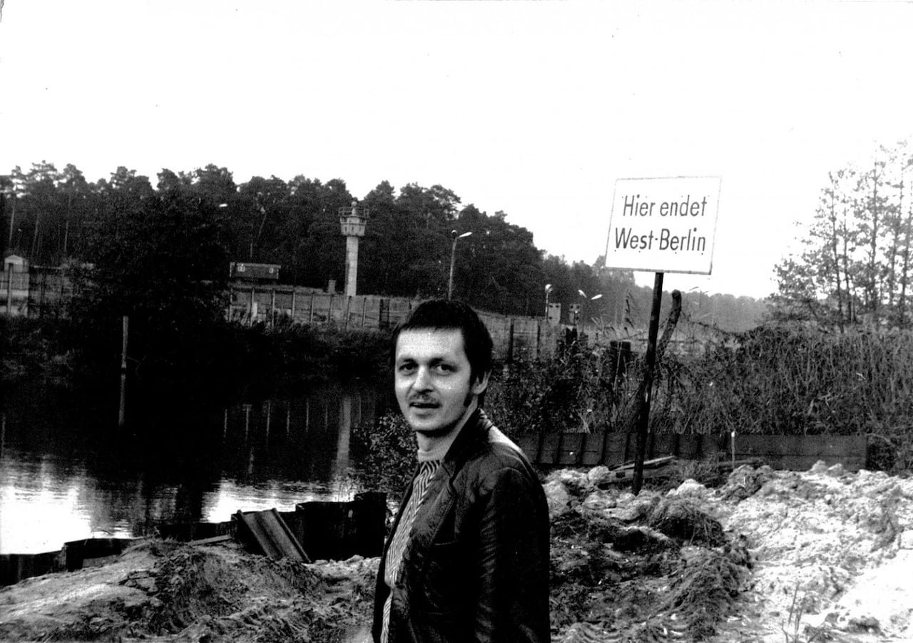 default-365 A man stands in front of the Spree river in black and white, with the Berlin wall behind him.