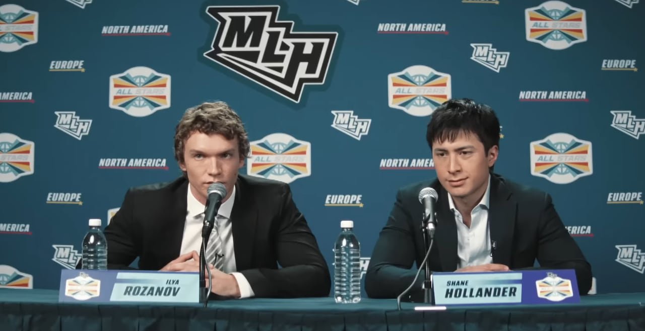 default-2 Two men sit down for a press conference. Both are wearing black blazers with white dress shirts underneath. Behind them is a series of logos