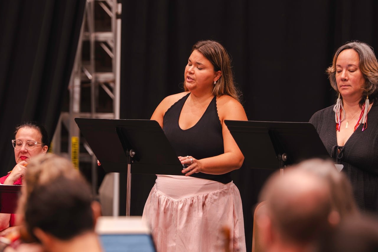 default-360 A woman in a pink dress and black halter top sings with a music stand before her, accompanied by another woman behind a music stand.