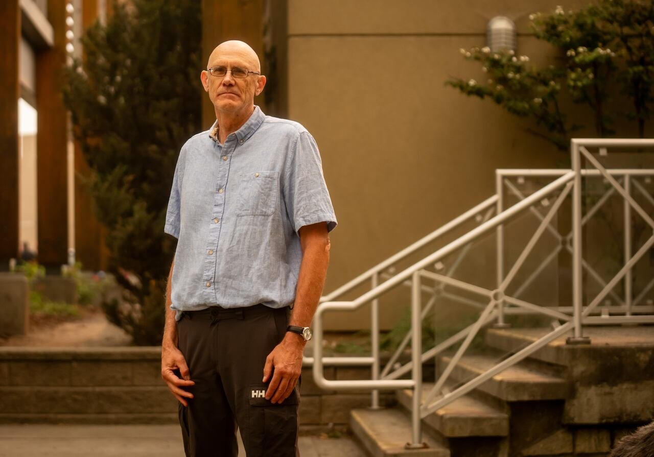 A bald man wearing a blue shirt is seen with smoke in the air.